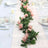 Pink rose garland centerpiece on a table setting with glassware and candles.
