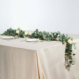 Elegant table setting with greenery and roses on a neutral tablecloth.