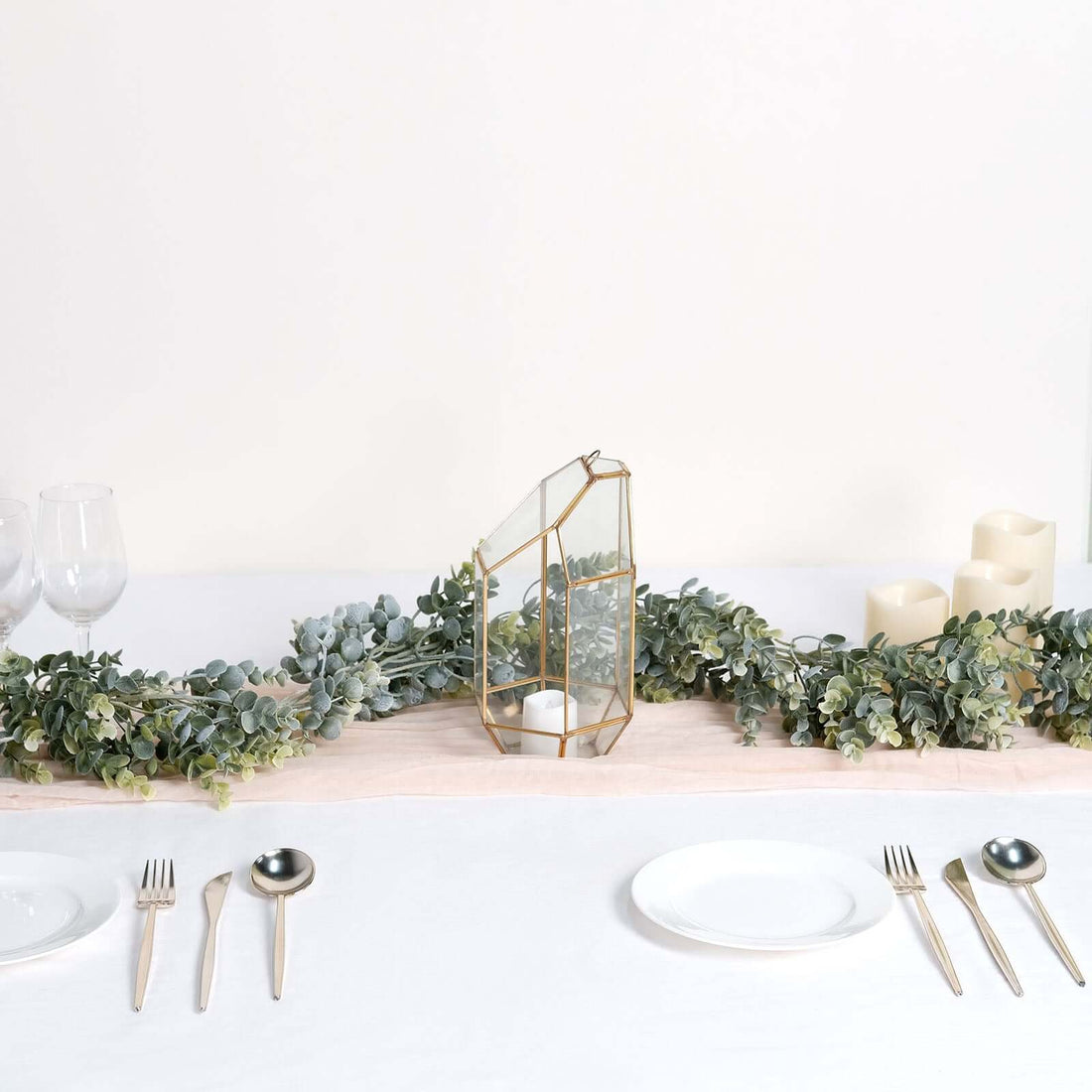 Gold geometric candle holder on a dining table with greenery and candles.