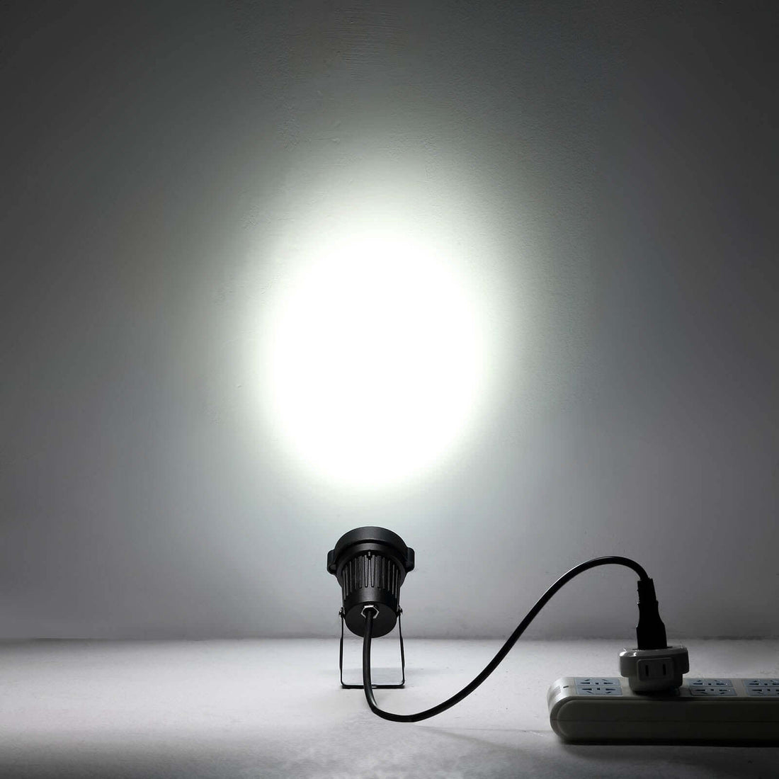 Black spotlight illuminating a white wall, plugged into a power strip. #whtbkgd