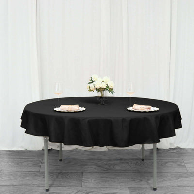 Round black tablecloth draped over a table set for two with wine glasses and flowers.