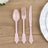 Elegant pink plastic cutlery set: spoon, fork, and knife on wooden table.