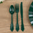 Green plastic cutlery set including spoon, fork, and knife on wooden surface.
