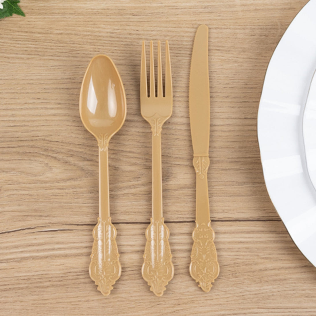 Elegant gold plastic cutlery set: spoon, fork, knife on wooden table.