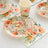 Floral disposable plates, cups, and napkins on a textured table setting.