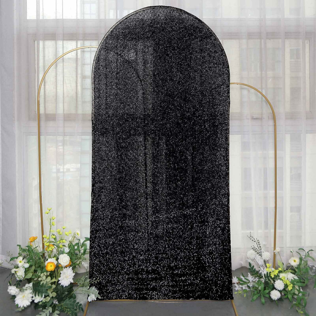 Black glitter backdrop with gold frame and floral arrangement.