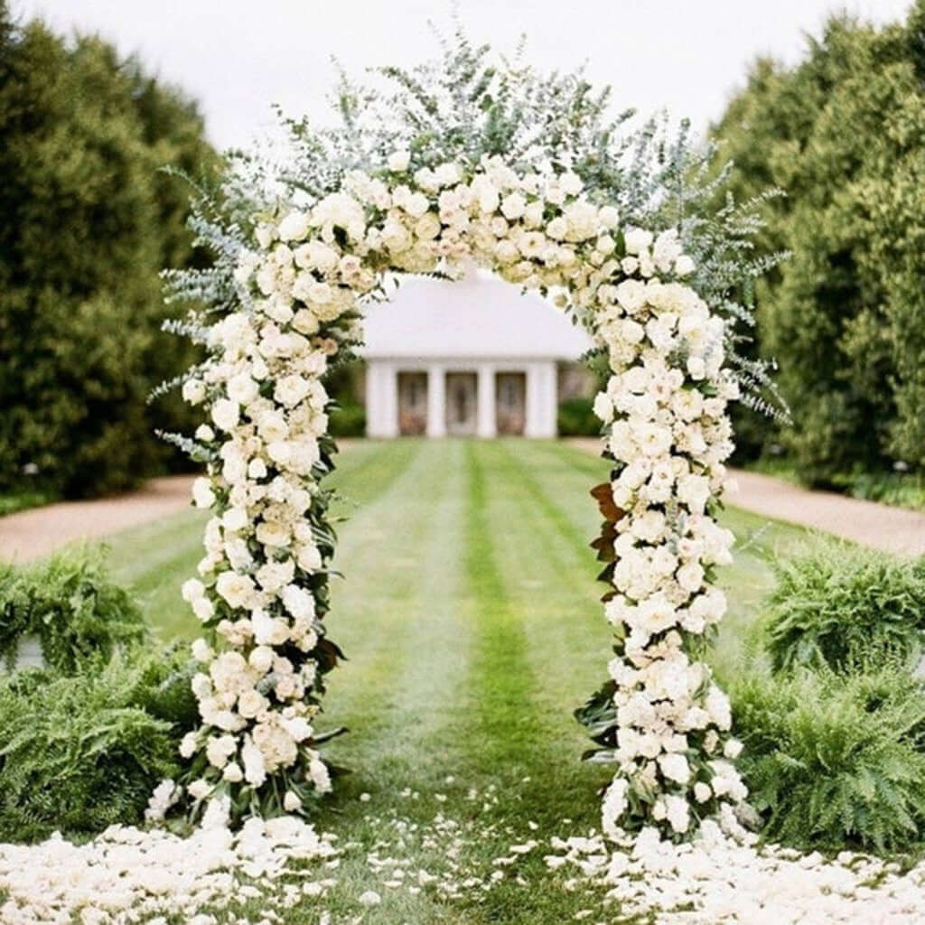 Floral wedding arch adorned with white flowers in a lush garden setting.