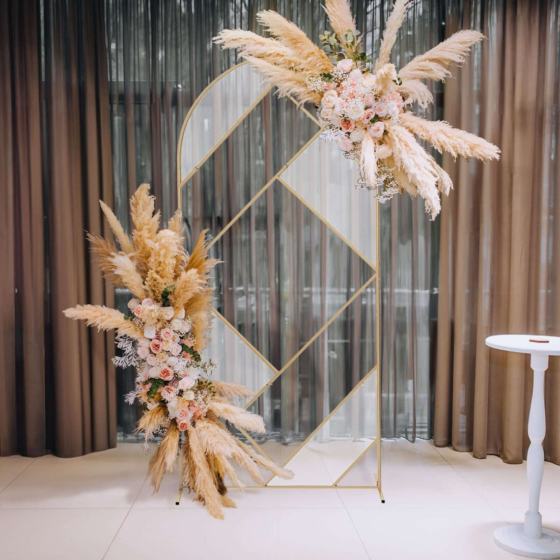 Decorative floral arch with pampas grass and roses in an elegant setting.