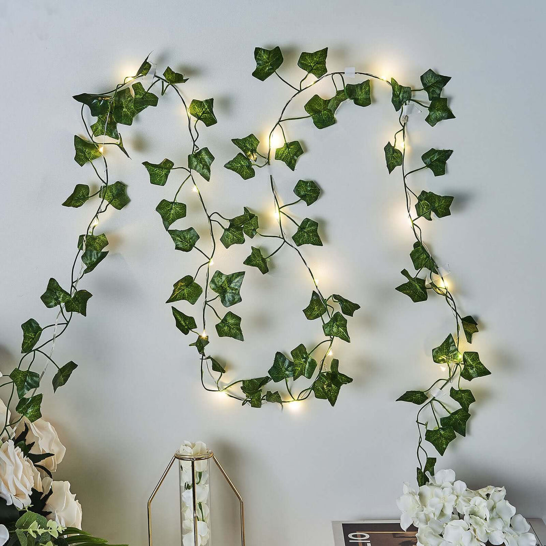 Artificial ivy garland with warm white fairy lights on a wall.