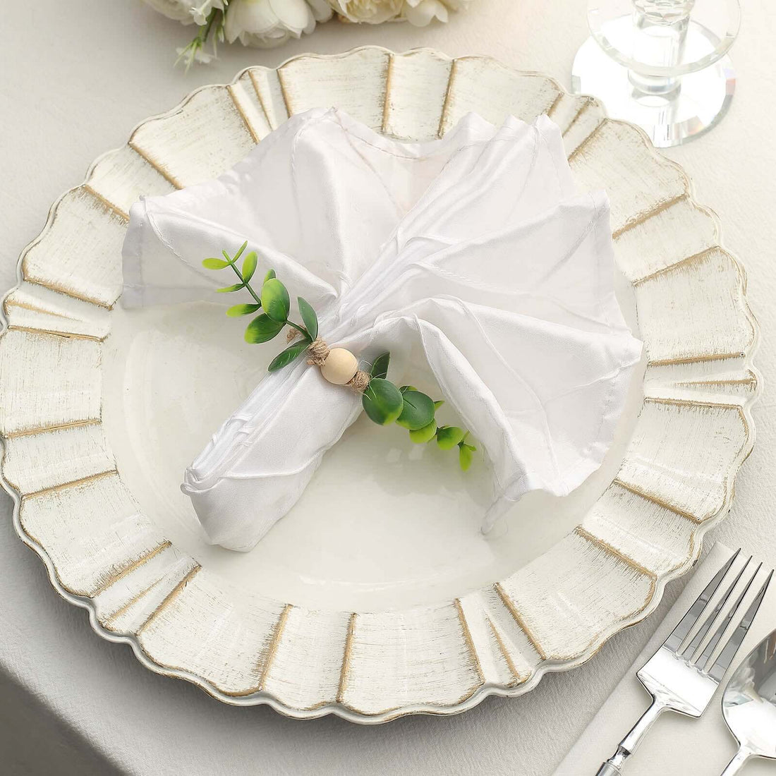 Elegant white napkin with greenery on decorative plate for table setting.