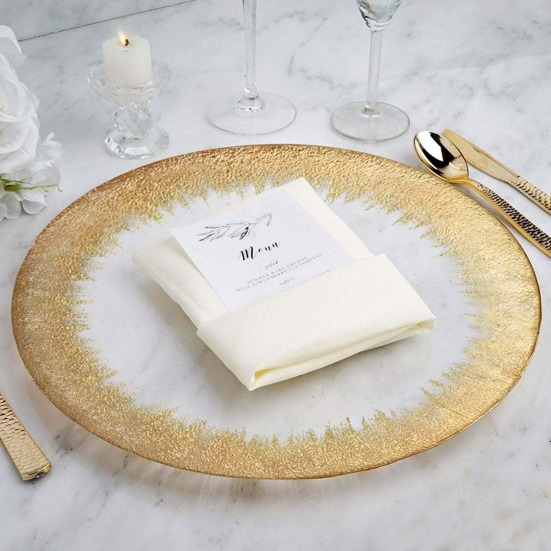 Elegant gold-rimmed plate with a folded napkin and menu card on a marble table.
