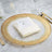 Elegant gold-rimmed plate with a folded napkin and menu card on a marble table.