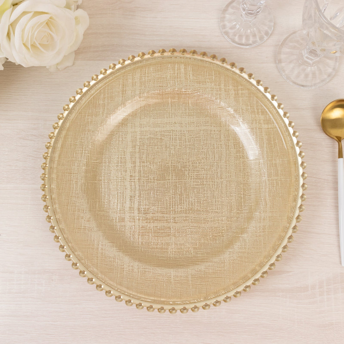 Gold textured charger plate with beaded edge on a light wood surface.