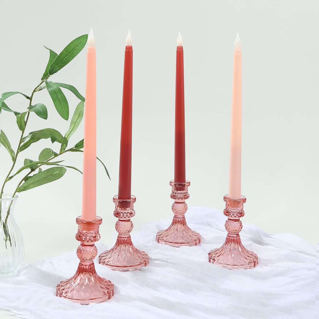 Set of four elegant candlesticks with tapered candles in pink and red hues.