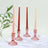 Set of four elegant candlesticks with tapered candles in pink and red hues.