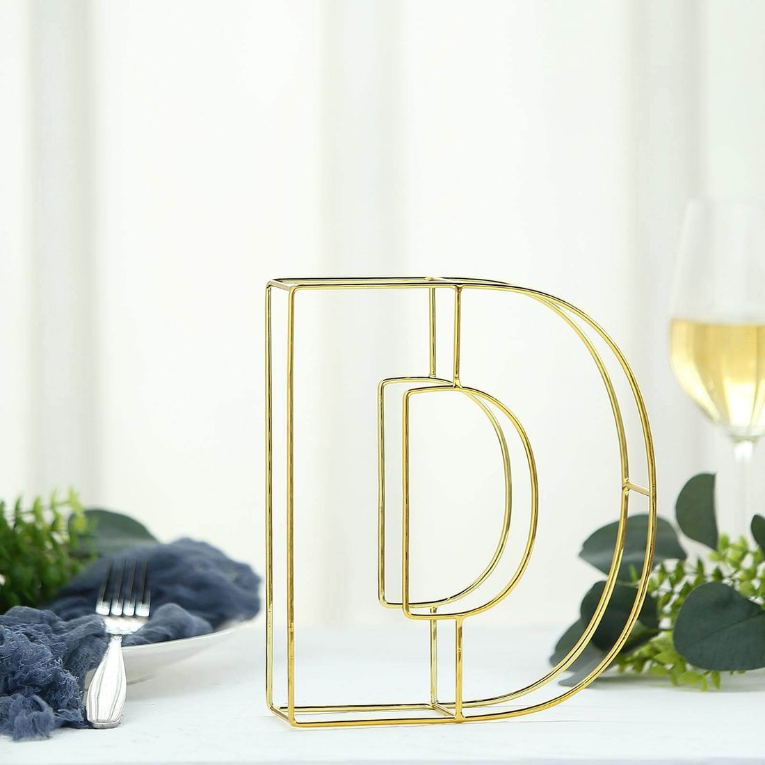 Gold wire letter "D" decorative piece on a dining table.