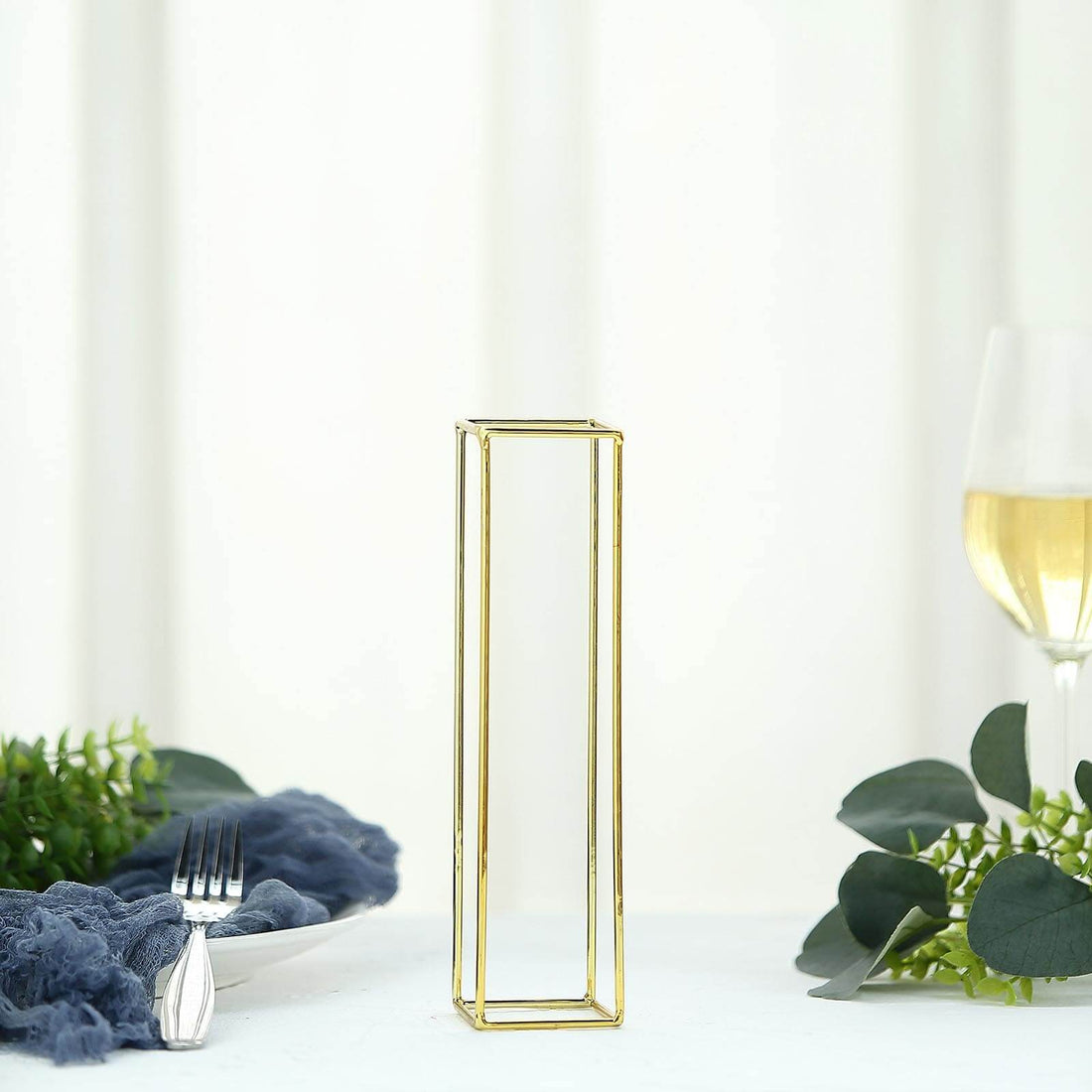 Gold geometric vase on a dining table with greenery and a wine glass.