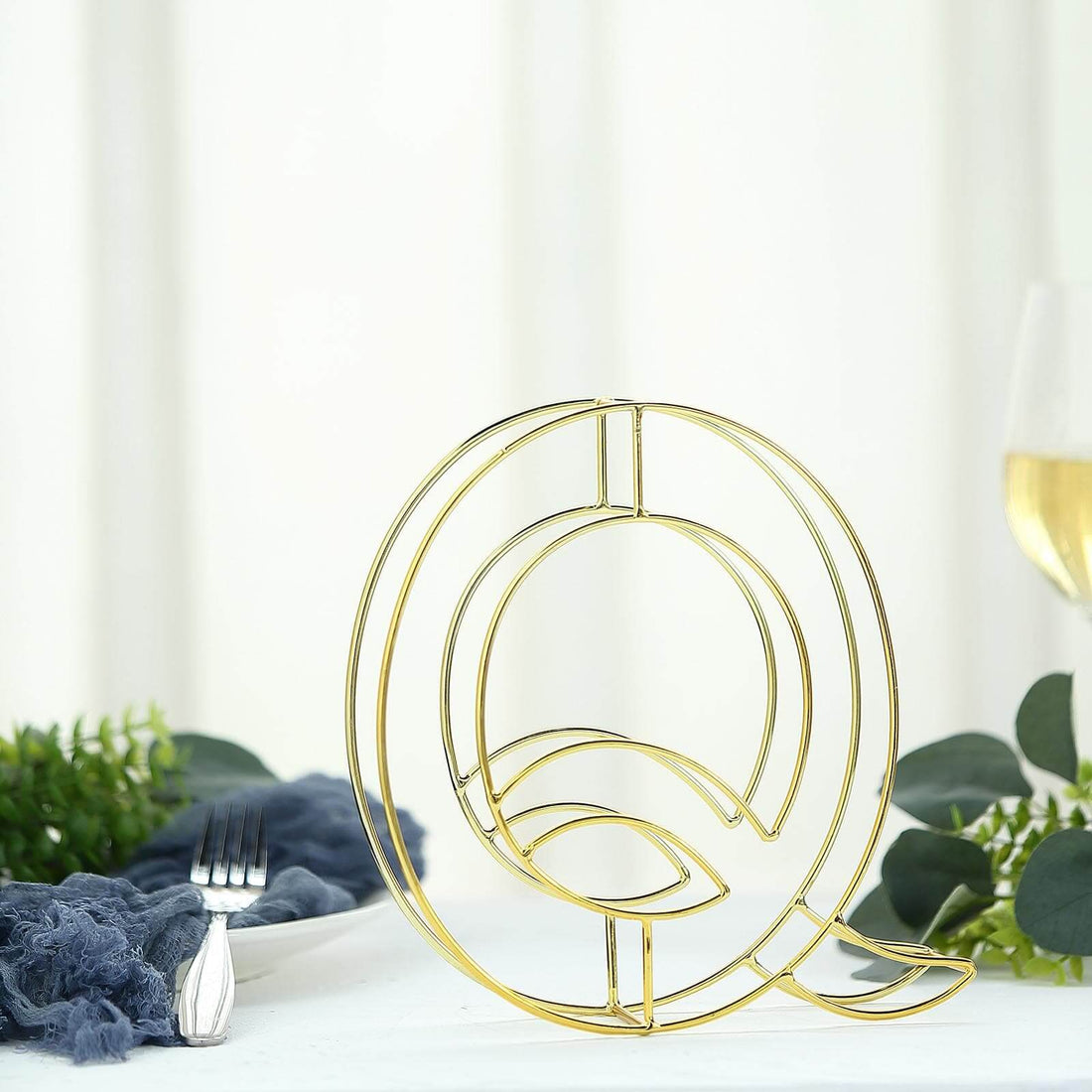 Gold abstract sculpture on a table with greenery and tableware.