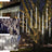 Decorative hanging LED light tubes illuminating tree branches at night.