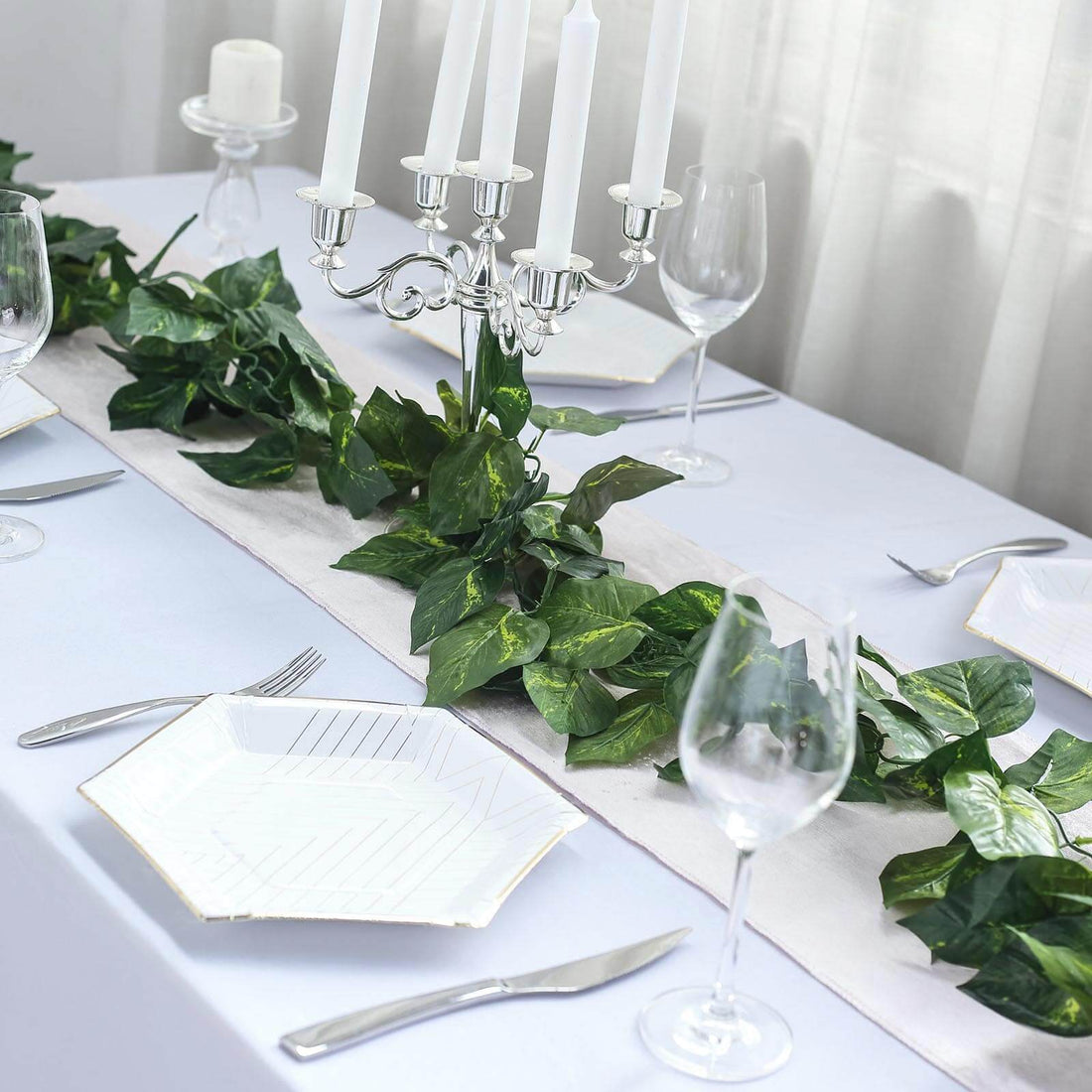Elegant dining table set with greenery, candles, and fine tableware.