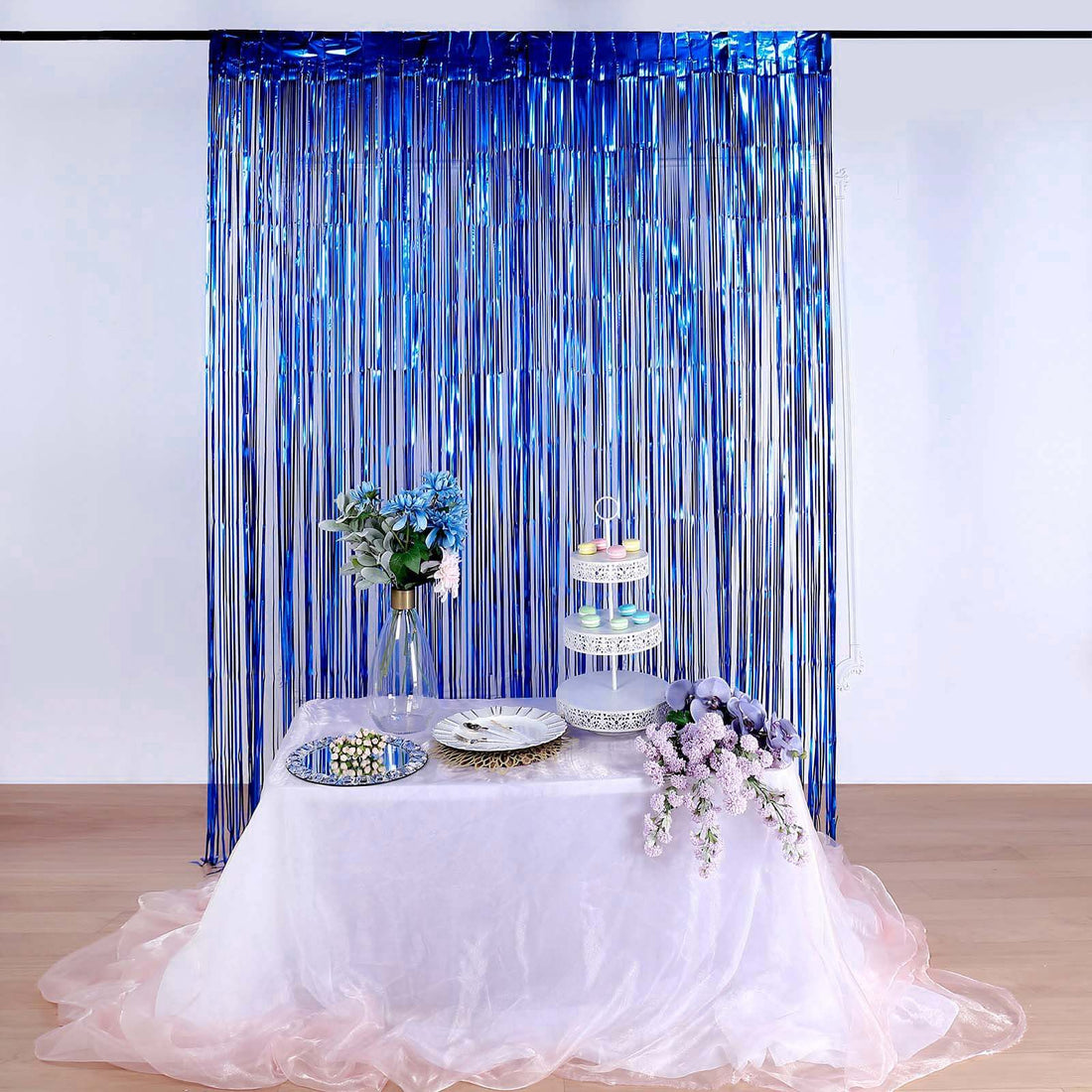 Decorative table setup with flowers, cake stand, and plates against a shimmering backdrop.