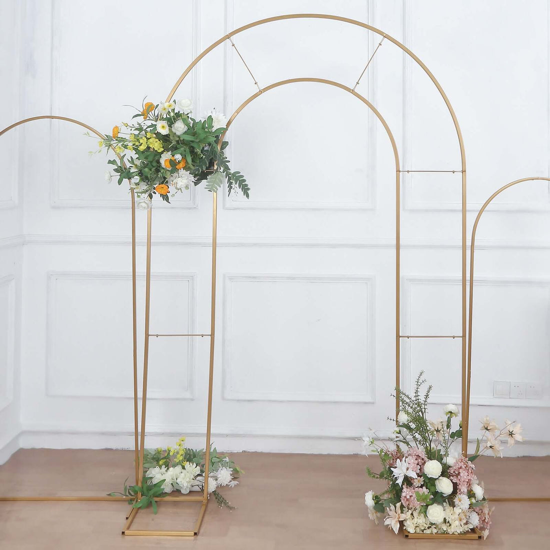 Gold wedding arch with floral arrangements on a plain backdrop.