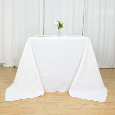 White tablecloth draping over a table with a vase of flowers on top.