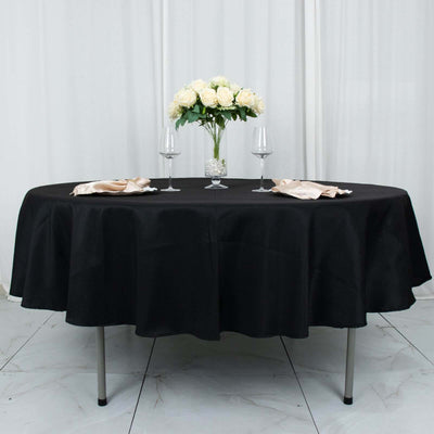 Black round tablecloth on a dining table set with flowers and glassware.