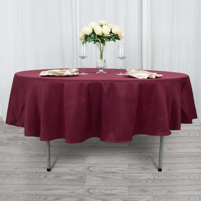 Burgundy round tablecloth on a table set for dining with flowers and glassware.