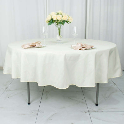 Elegant round table set with cream tablecloth, plates, napkins, and floral centerpiece.