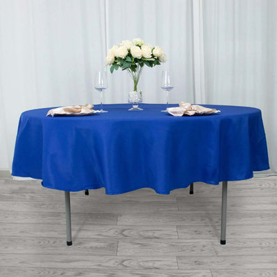 Round blue tablecloth on a table with floral centerpiece and wine glasses.