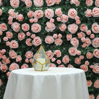 Geometric glass candle holder on a table with a floral backdrop of pink roses.