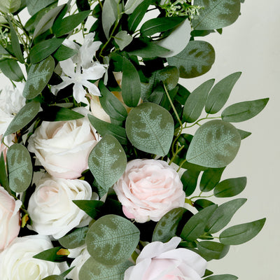 Artificial floral arrangement with pink and white roses surrounded by greenery.