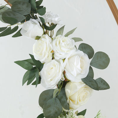 White artificial roses and greenery arrangement on a neutral backdrop.