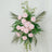 Artificial pink flower arrangement with greenery on a white backdrop.
