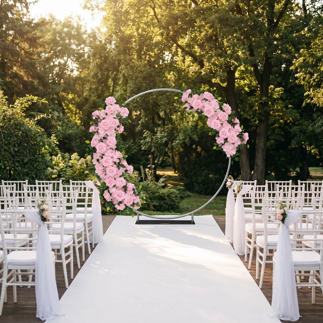 Outdoor wedding ceremony aisle with pink floral circle arch and white chairs