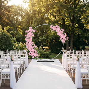 Outdoor wedding ceremony aisle with pink floral circle arch and white chairs