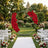 Outdoor wedding ceremony aisle with red rose floral arch and white chairs