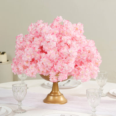 Pink floral centerpiece in a gold vase on a table.