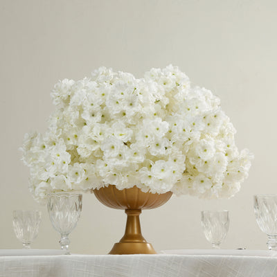 White floral arrangement in a gold vase with crystal glasses.