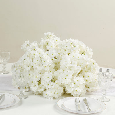 White floral centerpiece on a dining table with glassware and cutlery.