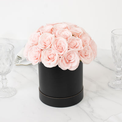 Black hat box filled with pink roses, elegantly displayed on a marble surface.