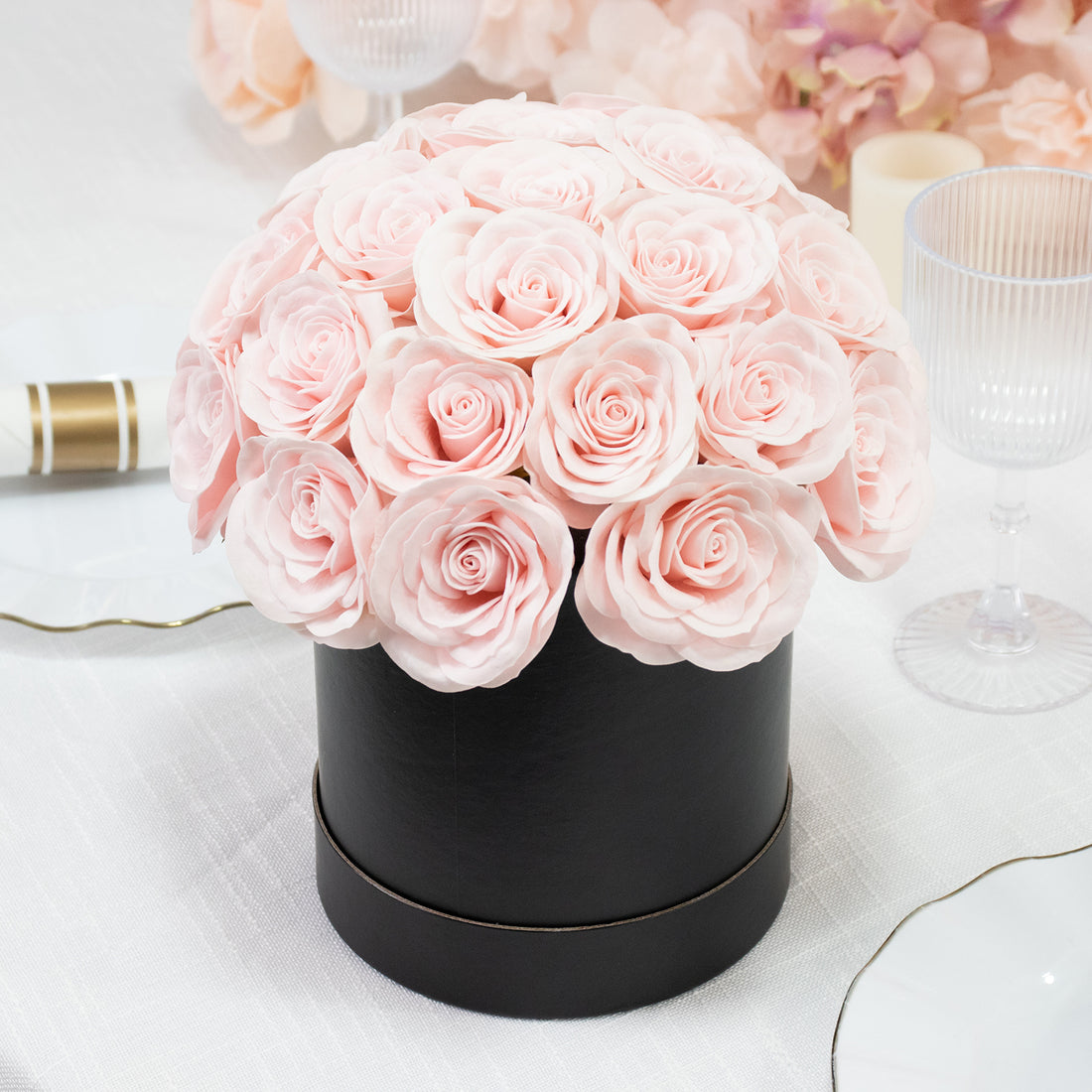 Pink rose bouquet in a black round box on a table setting.