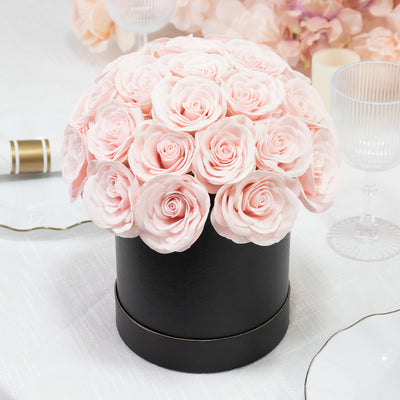 Pink rose bouquet in a black round box on a table setting.