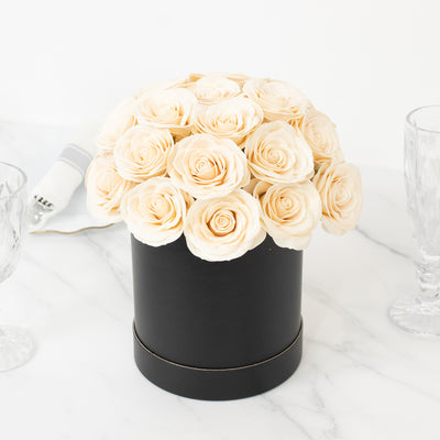 Elegant cream rose bouquet in a black round box on a marble surface.