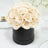 Cream rose bouquet in a black round box on a table setting.