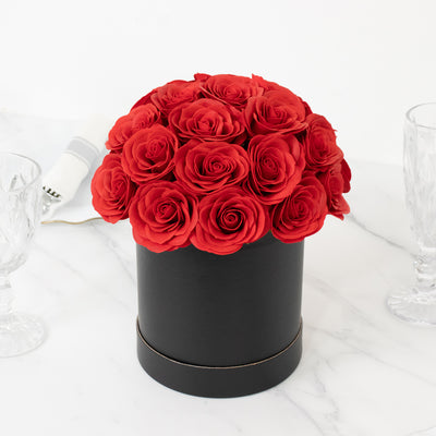Red rose bouquet in a black cylindrical vase on a marble surface.
