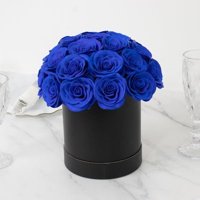 Blue rose arrangement in a black round box on a marble surface.