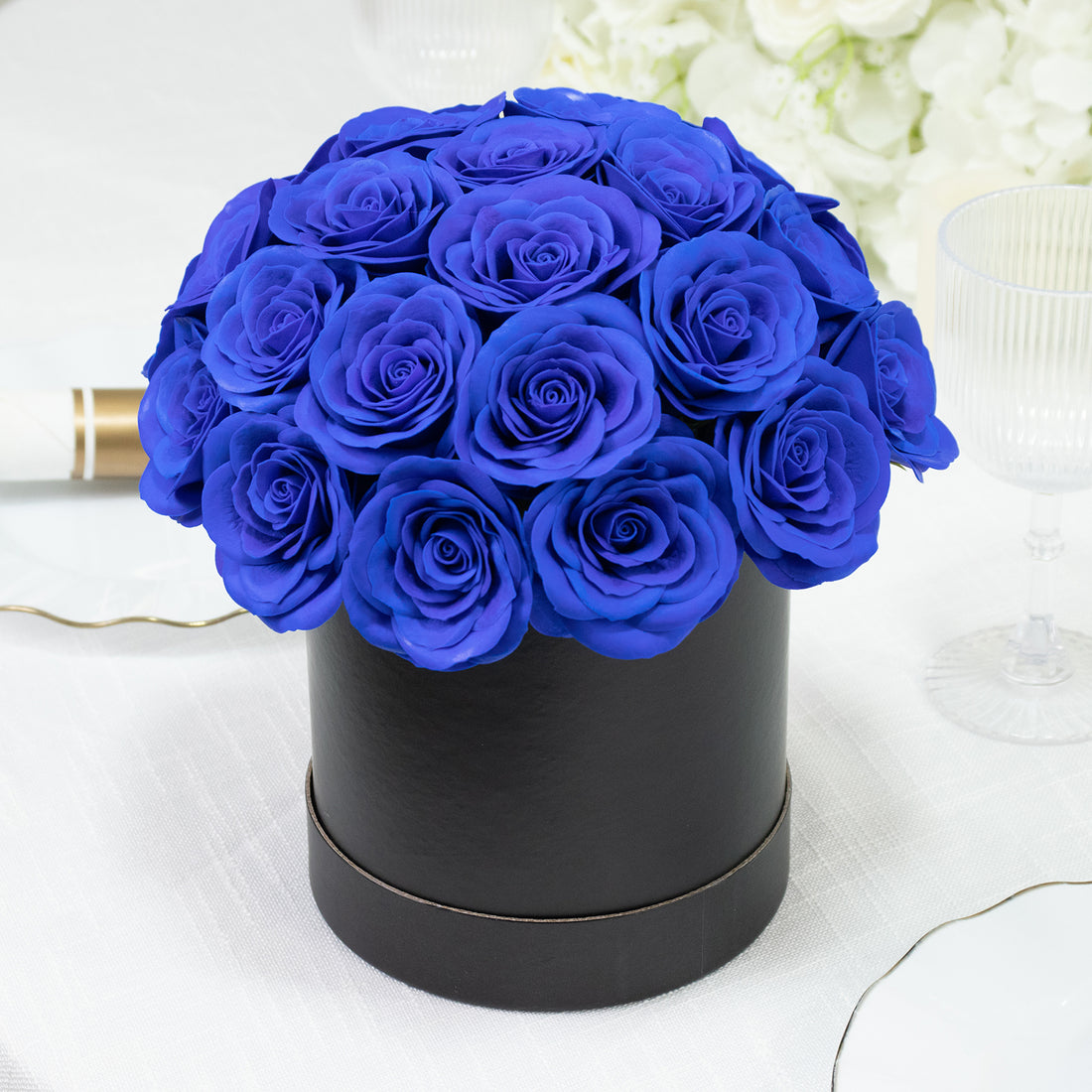 Blue rose bouquet in a black round box on a white table setting.