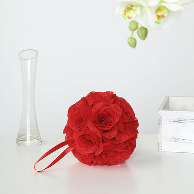 Red floral arrangement with ribbon handle on a white table.